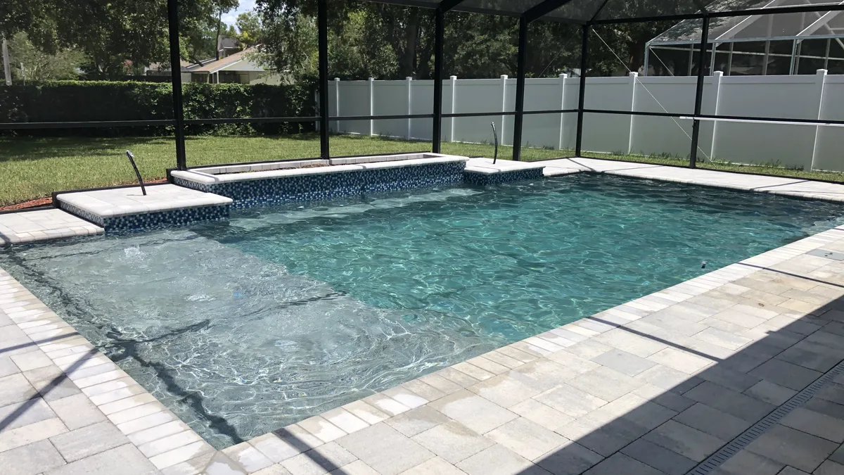 Geometric pool with sun shelf, spa, and travertine deck inside screen enclosure, Trinity FL